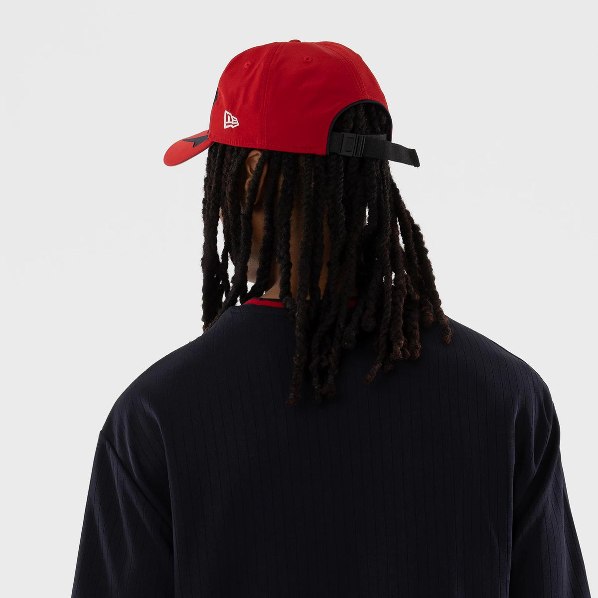 New Era Sultanes De Monterrey LMB Navy Oversized T-Shirt, back view on a model featuring a ribbed neckline in red, worn with a red cap displaying an embroidered New Era logo on the side, showing a relaxed fit and vertical stripes on the navy fabric.