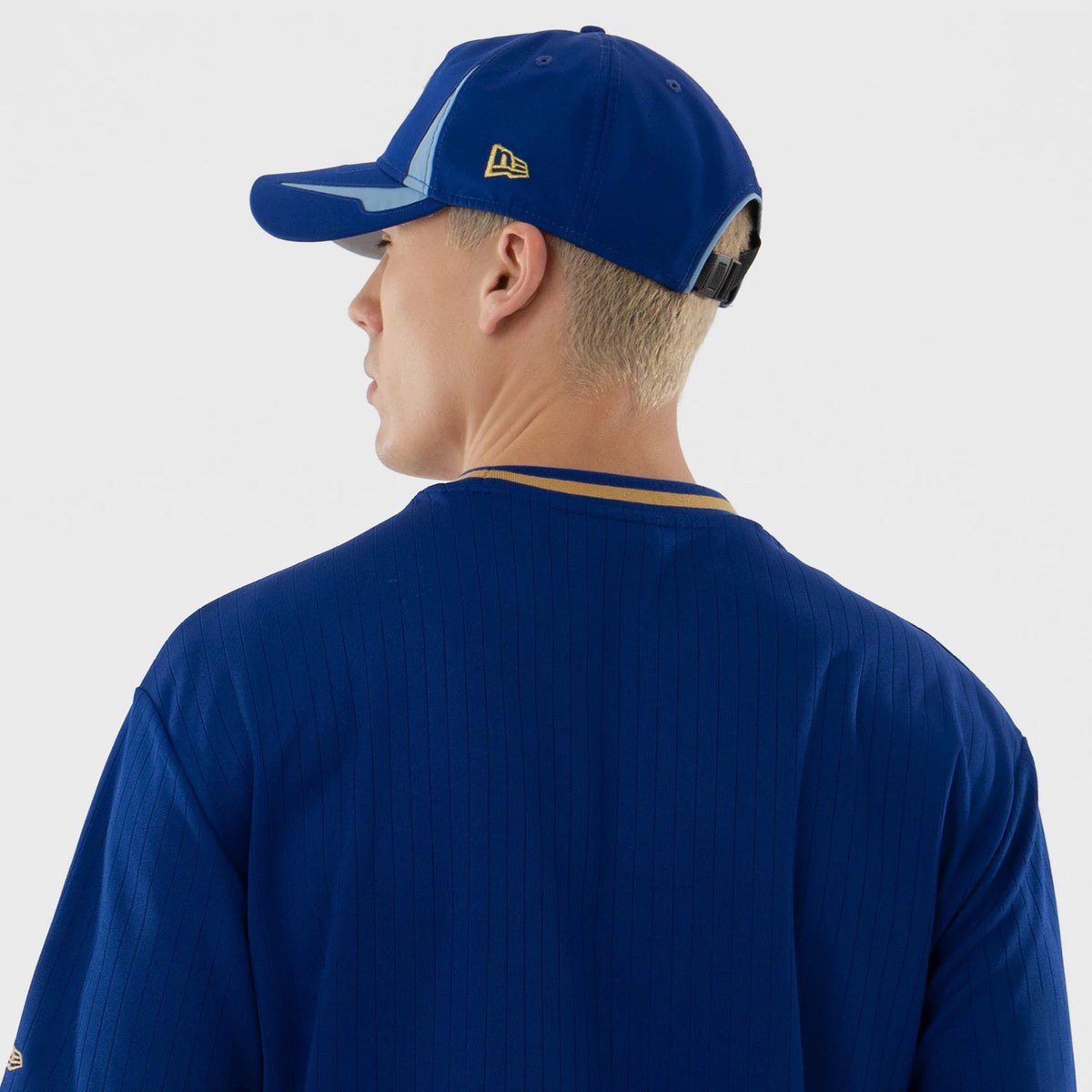 New Era Kansas City Royals MLB Blue Oversized T-Shirt, back view on a model also wearing a blue cap showing thin vertical stripes down the shirt, contrasting yellow trim around the neckline, and a small embroidered New Era logo on the cap side.