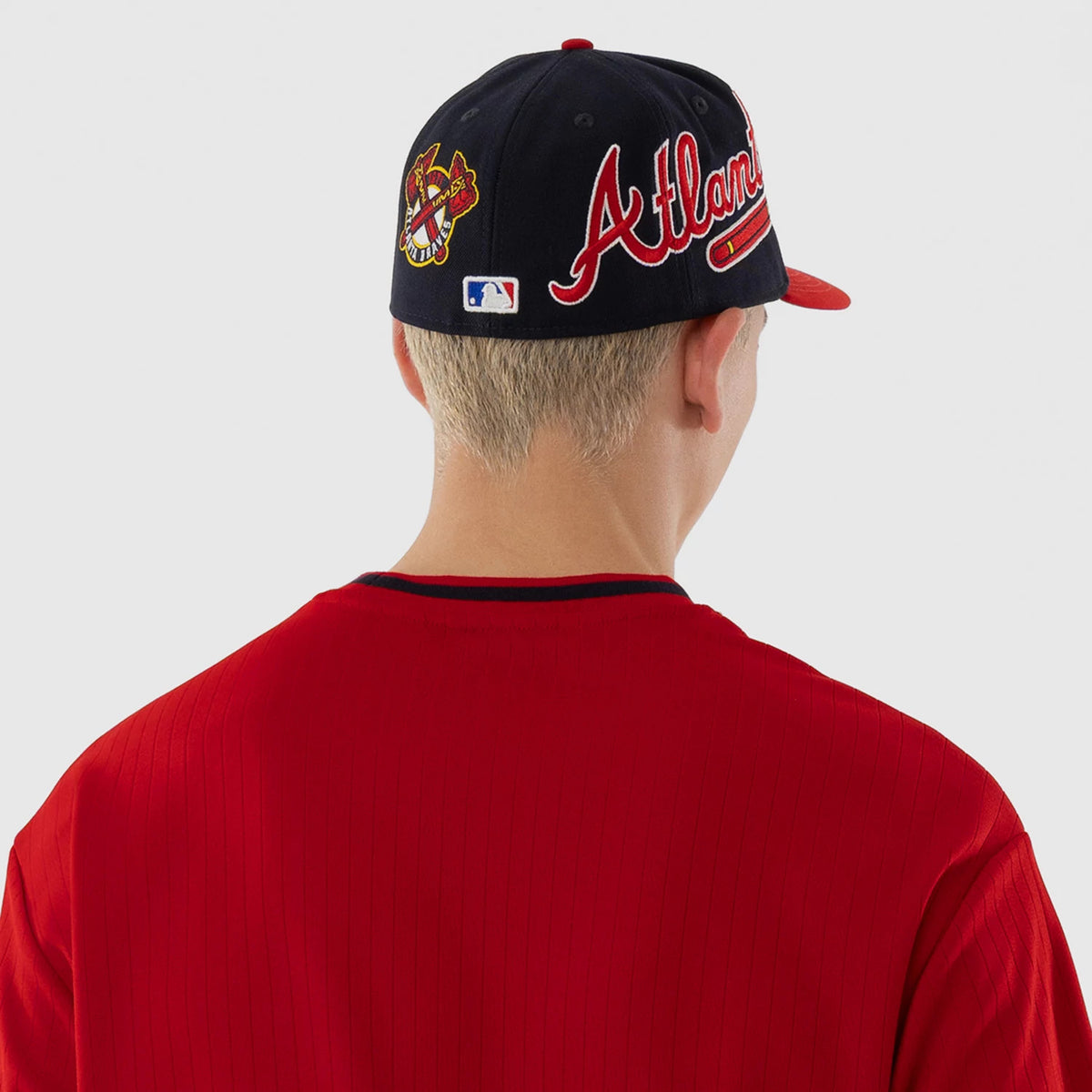 New Era Atlanta Braves MLB Red Oversized T-Shirt, back view on a model wearing a matching cap, showing the clean red fabric with discreet seam lines, contrast black trim at the neckline, and the cap featuring an embroidered Atlanta script.