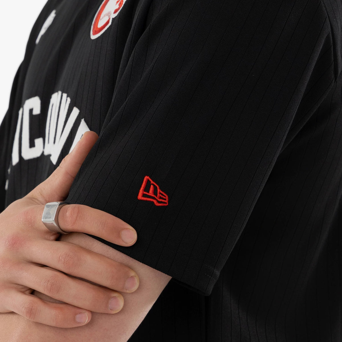 New Era Vancouver Canadians MiLB Black Oversized T-Shirt, close-up view featuring the white Vancouver lettering across the chest, red embroidered New Era logo on the sleeve, and vertical stripe texture on the fabric.