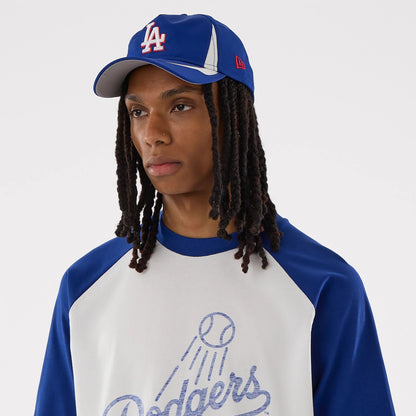New Era LA Dodgers MLB White Boxy T-Shirt, on-model front view highlighting the large Dodgers script with a decorative baseball graphic on the chest, blue raglan sleeves, and styled with a two-tone blue and white cap featuring an embroidered LA logo.