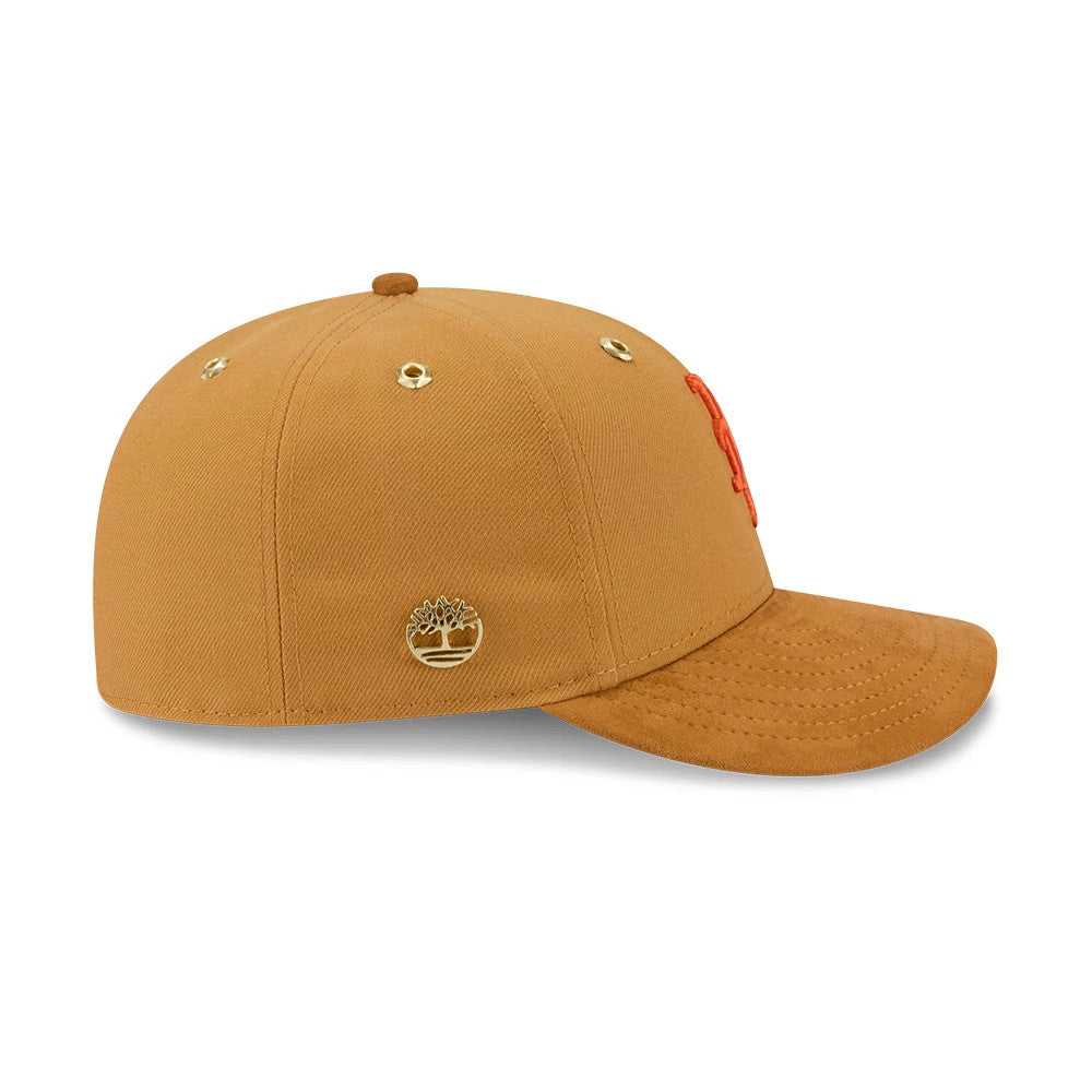 New York Mets Timberland X MLB Panama Tan New Era 59FIFTY Fitted Cap, side view showing the gold Timberland tree logo embroidered on the tan crown, the matching gold eyelets, and an orange Mets logo in raised embroidery on the front panel.