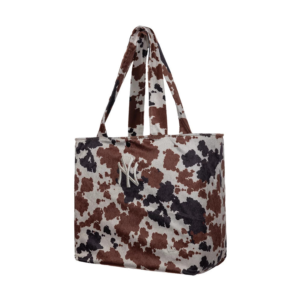 New Era New York Yankees MLB Cow Print Tote Bag, three-quarter view showing a spacious rectangular brown and black cow print design with two handles, an embroidered New York Yankees logo on the front, and a printed New Era logo near the base.