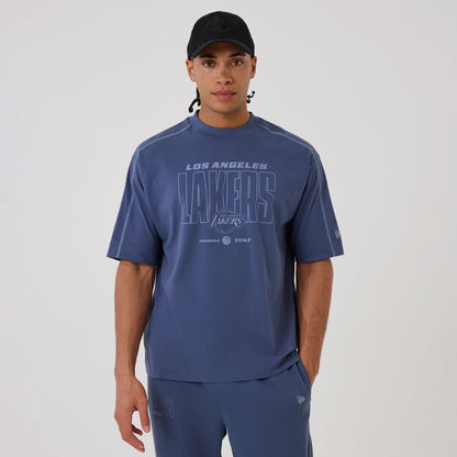 New Era LA Lakers NBA Graphic Dark Blue Boxy T-Shirt, front view on-model showcasing a large printed Lakers logo across the chest, with 'Los Angeles' lettering above, complemented by a New Era logo embroidered on the left sleeve.