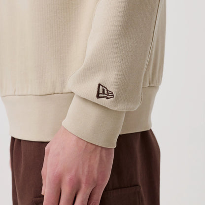 New Era Philadelphia Phillies MLB Arch Graphic Light Beige Crew Neck Sweater, side view on a model showing the ribbed cuff with a brown embroidered New Era flag logo on the sleeve, paired with brown trousers for a casual look.