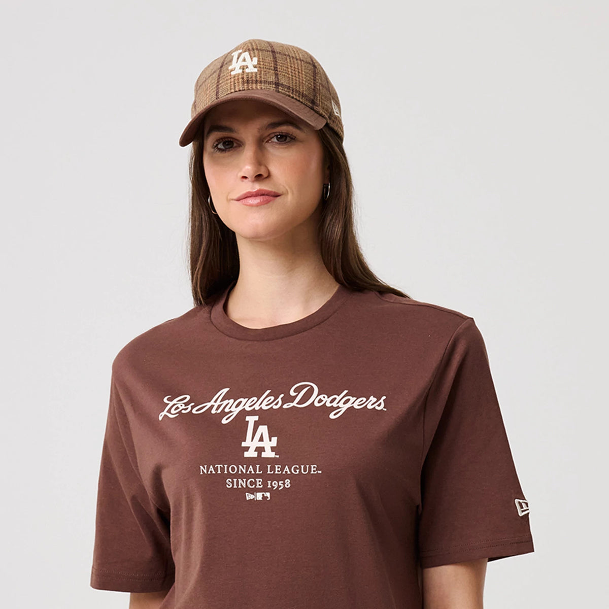 New Era LA Dodgers MLB Linear Brown T-Shirt, front view on-model with a matching checked cap, features the white embroidered Los Angeles Dodgers script and LA logo on the chest, while the New Era flag logo is printed on the sleeve.