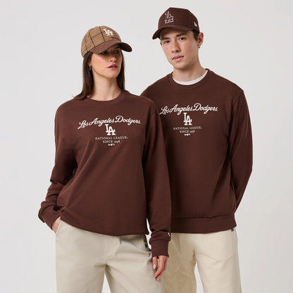 New Era LA Dodgers MLB Linear Brown Crew Neck Sweater, front view on a model with a matching brown cap, featuring the white embroidered Los Angeles Dodgers script and LA logo on the chest, with ribbed cuffs and hem.