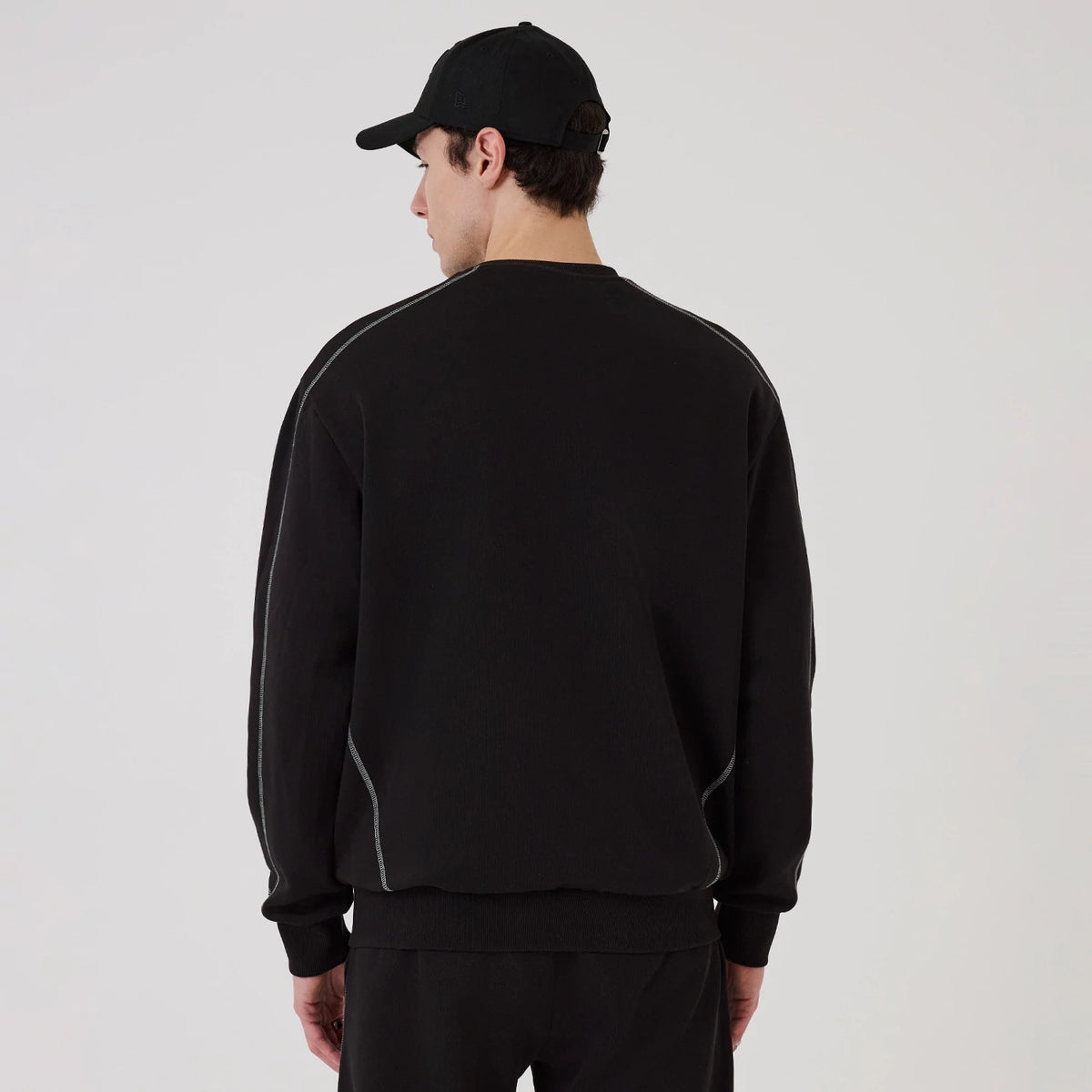 New Era Chicago Bulls NBA Graphic Black Crew Neck Sweater, back view on a model wearing a black cap, showing the sweater's black fabric with grey piping along the shoulders and side seams, and a relaxed fit at the hem and cuffs.