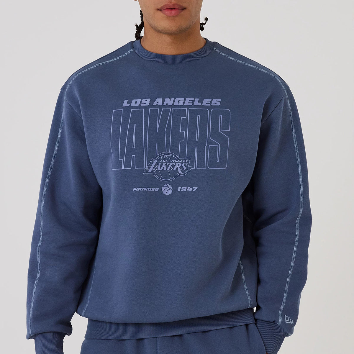 New Era LA Lakers NBA Graphic Dark Blue Crew Neck Sweater, front view on a model featuring large embroidered Los Angeles Lakers lettering across the chest, a basketball graphic with Founded 1947 below, and ribbing at the cuffs and waistband.