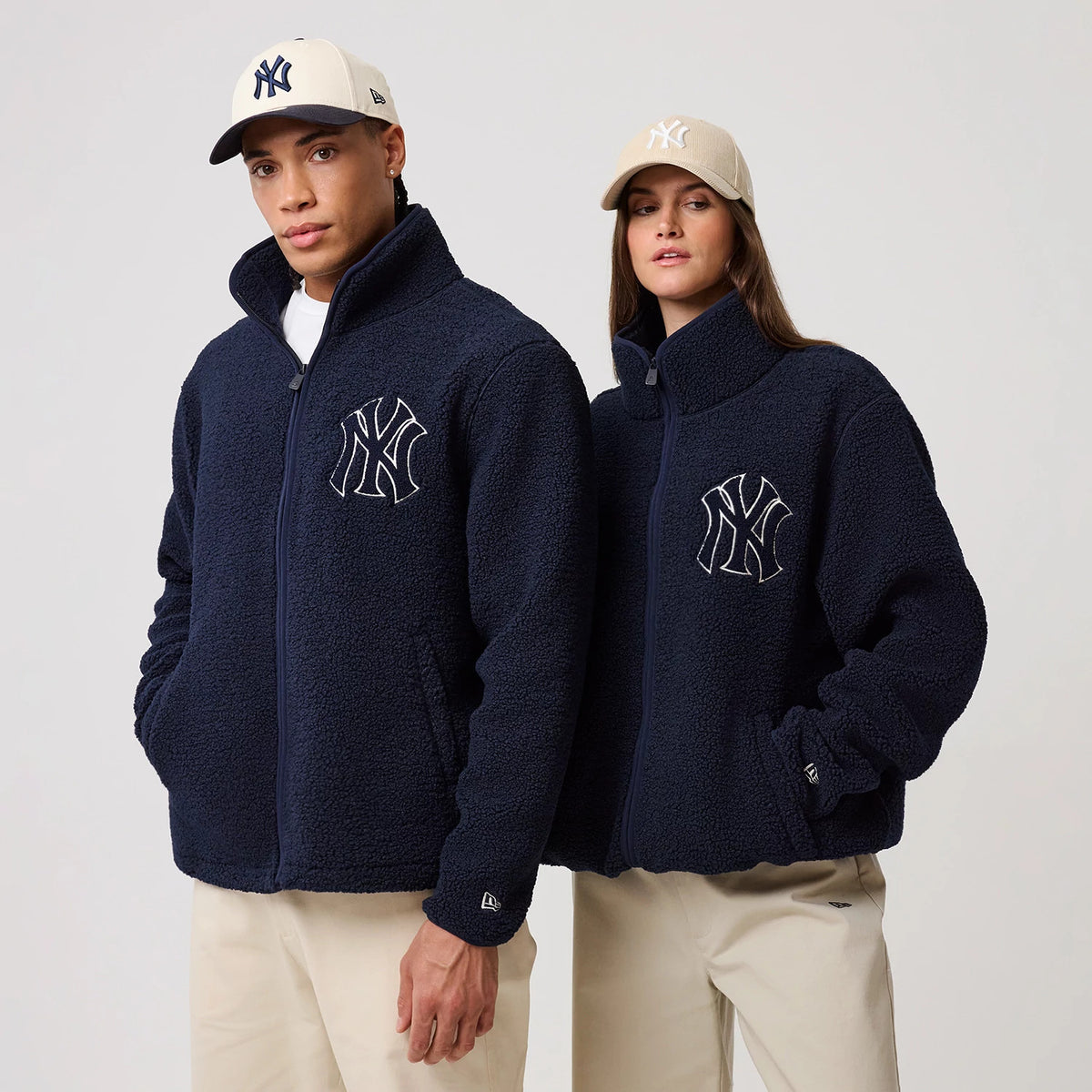 New Era New York Yankees MLB Dark Blue Sherpa Jacket, front view on models featuring a prominent raised New York Yankees logo on the left chest, full zip closure, and the New Era logo embroidered on the left cuff; styled with beige trousers.