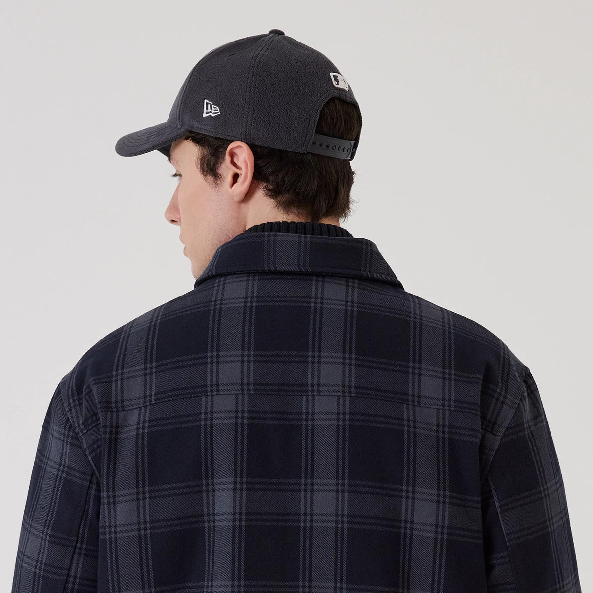 New Era Navy Shacket, rear view on a model with a structured design, featuring a checkered pattern in dark navy tones, complemented by long sleeves and a collar, with the model also wearing a dark grey New Era cap.