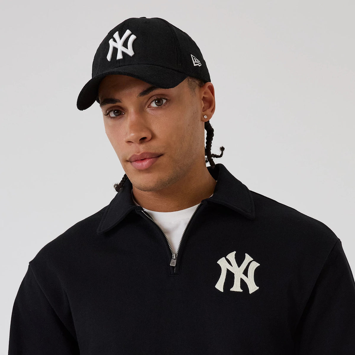New Era New York Yankees MLB Black 1/4 Zip Sweater, front view on a model paired with a black Yankees cap, featuring an embroidered white NY logo on the left chest, complementing the cap's curved visor and New Era flag logo on the side.