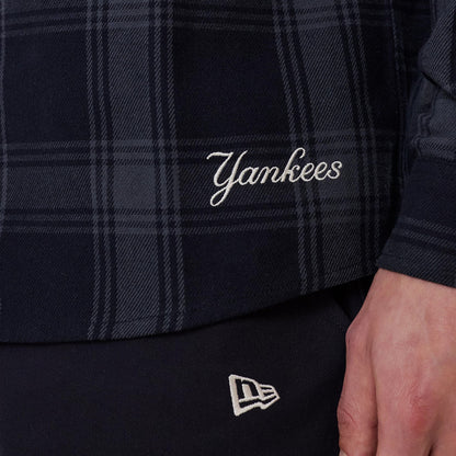 New Era New York Yankees MLB Plaid Navy Long Sleeve Shirt, close-up view showing the white 'Yankees' script embroidery on the lower part of the plaid pattern, with a glimpse of the New Era flag logo on black trousers beneath.