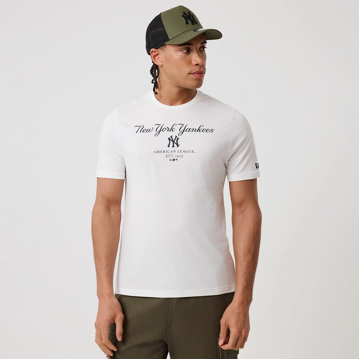 New Era New York Yankees MLB Linear White T-Shirt, front view on a model displaying a black printed script logo and American League Est. 1903 text across the chest, an embroidered New Era flag on the left sleeve, paired with olive trousers.