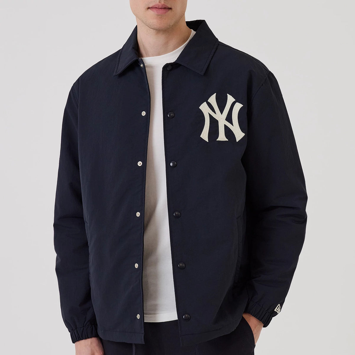 New Era New York Yankees MLB Navy Coach Jacket, front view on a model showing a navy jacket with a large embroidered white New York Yankees logo on the left chest, black snap-button closures, and a small embroidered New Era logo on the left cuff.