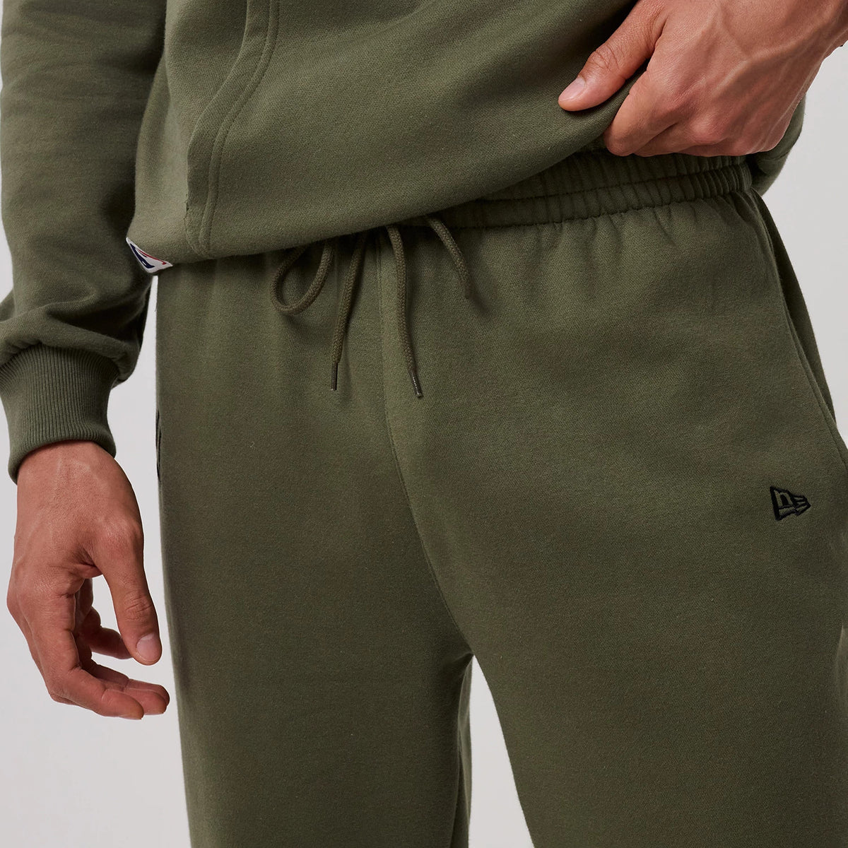 New Era New York Yankees MLB League Essential Green Joggers, on-model close-up showing the comfortable elastic waistband with adjustable drawstrings, a black embroidered New Era flag logo on the right thigh.
