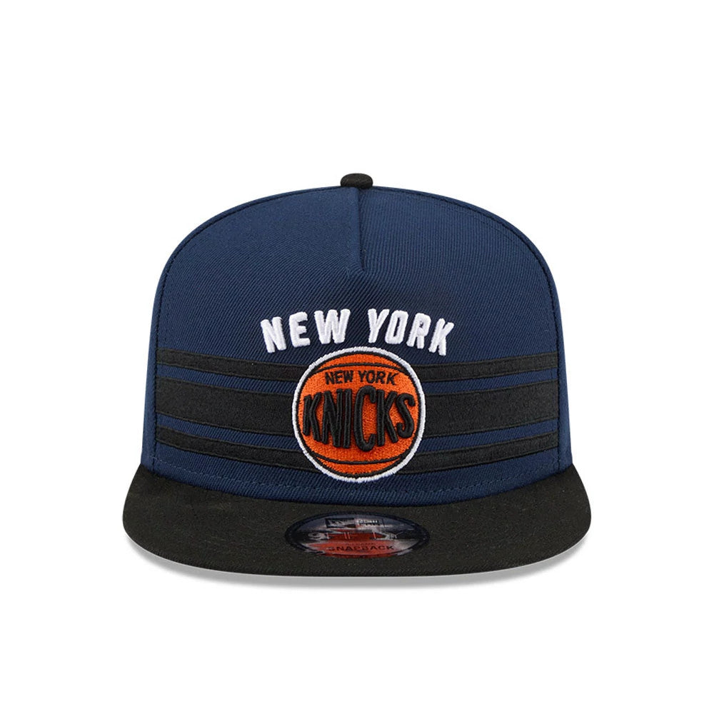 New York Knicks NBA Tip Off 2026 Dark Blue New Era 9FIFTY A-Frame Snapback Adjustable Cap, front view showing the New York Knicks logo with raised orange basketball embroidery on the dark blue crown.