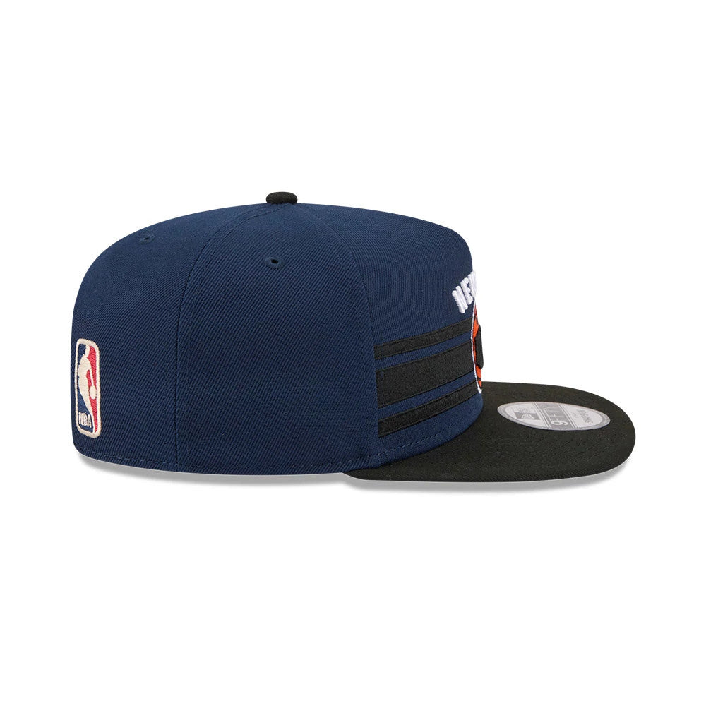 New York Knicks NBA Tip Off 2026 Dark Blue New Era 9FIFTY A-Frame Snapback Adjustable Cap, side view showing the NBA logo on the left side of the structured dark blue crown, with black stripes and a black flat visor.