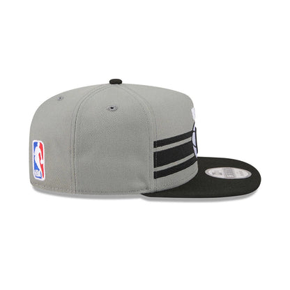 Brooklyn Nets NBA Tip Off 2026 Dark Grey New Era 9FIFTY A-Frame Snapback Adjustable Cap, side view showing the NBA logo embroidered on the left side, with a black flat visor and parallel black stripes across the structured dark grey crown.