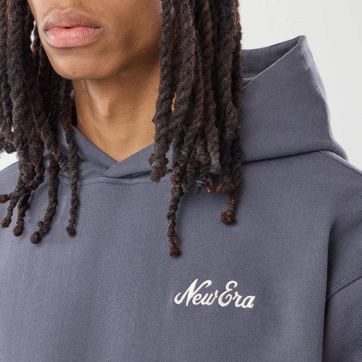 New Era Open Hem Grey Pullover Hoodie, front view on a model showing the grey fabric with a relaxed fit, an embroidered white New Era logo on the left chest, and a spacious hood draping naturally behind the head.