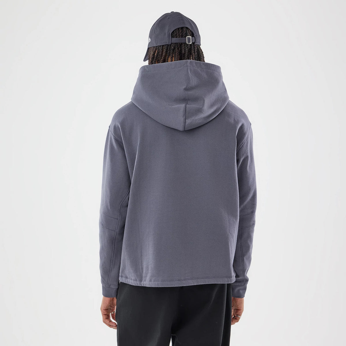 New Era Open Hem Grey Pullover Hoodie, back view on a model wearing a matching grey cap, showcasing the relaxed fit and the hood falling naturally on the shoulders, with the open hem providing a casual, loose silhouette.