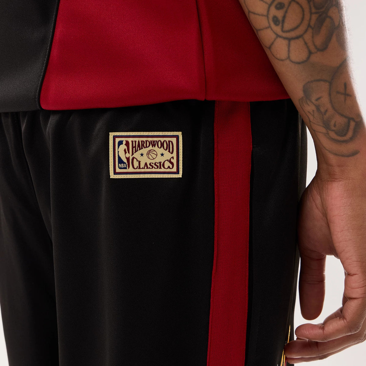 New Era Miami Heat NBA Hardwood Classic Straight Black Straight Leg Joggers, close-up view on a model showing the embroidered NBA Hardwood Classics logo on the right leg, with a red side stripe and black fabric extending downwards.