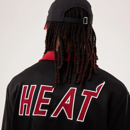 New Era Miami Heat NBA Hardwood Classic Revere Black Short Sleeve Shirt, back view on a model showing the large red and white embroidered HEAT lettering across the upper back, complemented by a black cap with an adjustable strap.