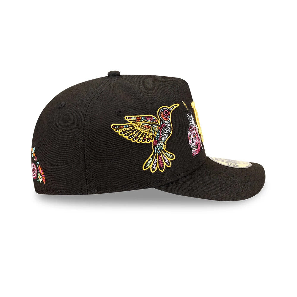 LA Dodgers MLB Day Of The Dead Black New Era 59FIFTY A-Frame Fitted Cap, side view showing embroidered designs including a colourful hummingbird and skull on the structured black crown, complemented by a flat visor with a 59FIFTY size sticker.