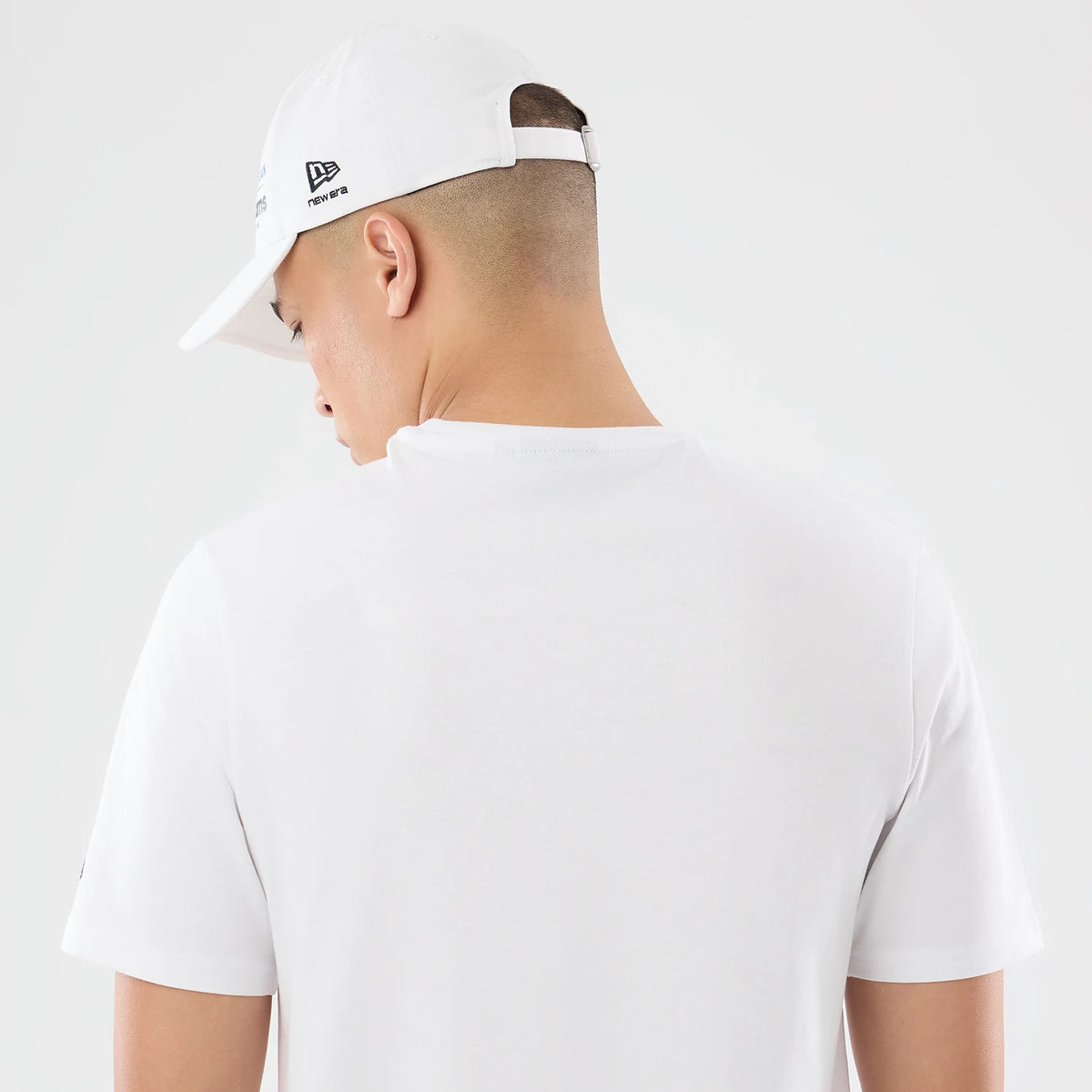 New Era Williams Carlos Sainz Spain Race Special White T-Shirt, back view on-model showing a plain white fabric with short sleeves, accompanied by a white cap featuring an embroidered New Era logo and raised design on the side.