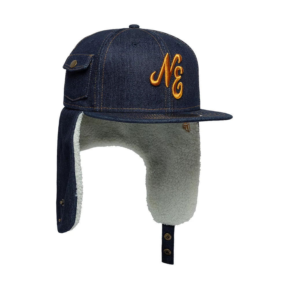 New Era Denim Navy Dogear 59FIFTY Fitted Cap, side view showing a raised orange NE embroidery on the navy denim front panel, with buttoned pocket detail on the left side and fleece-lined dogear flaps hanging down.