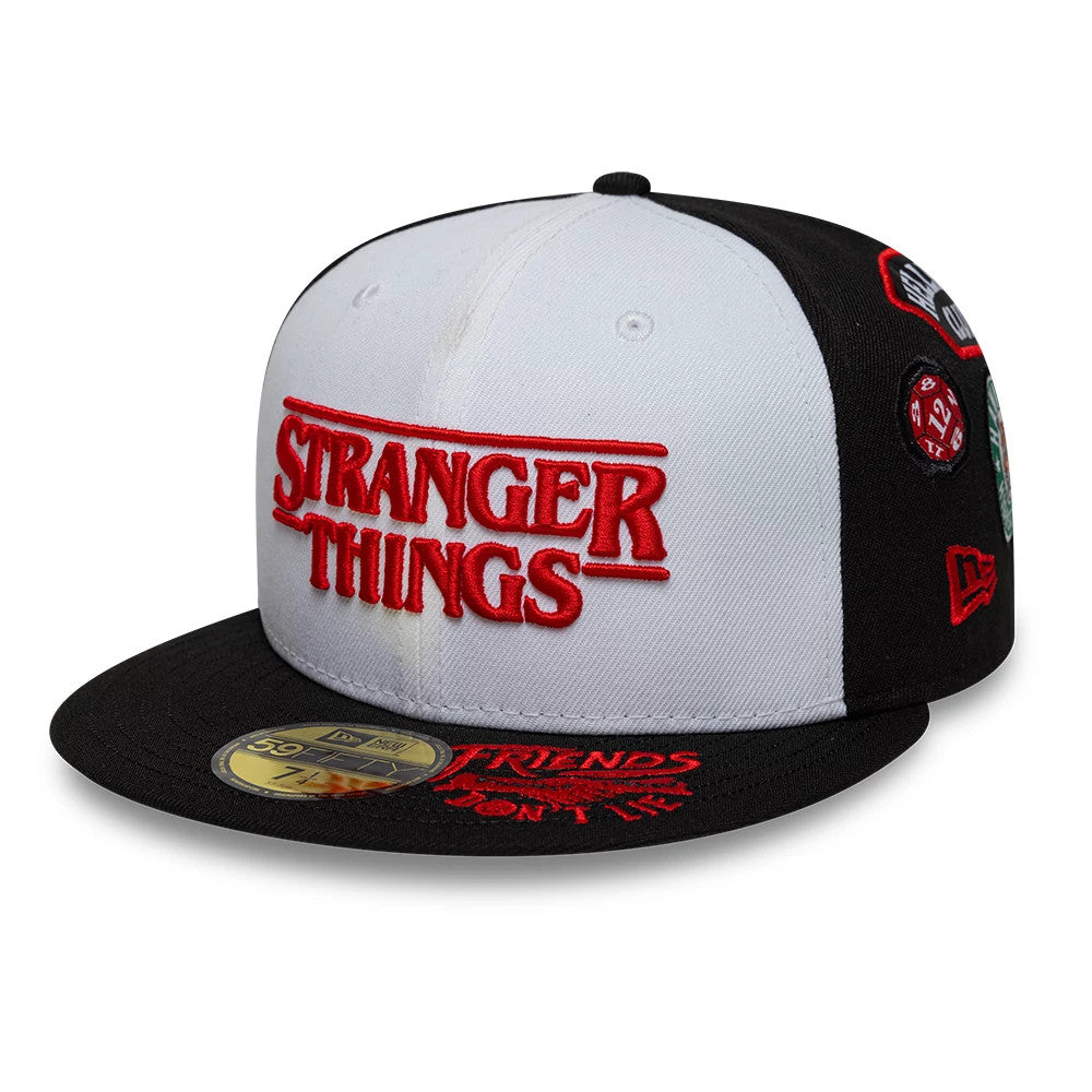 Netflix Stranger Things 10 Years Black New Era 59FIFTY Fitted Cap, front view showing red raised embroidery of Stranger Things on the white front panel, a black flat visor with a gold 59FIFTY size sticker, and multiple patches on the side.