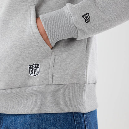 New Era Jacksonville Jaguars NFL Patch Grey Pullover Hoodie, side view showing a person's hand in the front pocket, a white printed NFL logo near the hem, and an embroidered logo on the ribbed cuff of the left sleeve above blue jeans.