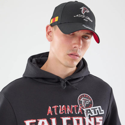 New Era Atlanta Falcons NFL Patch Black Pullover Hoodie, front view on-model highlighting the printed Atlanta Falcons logo and team name across the chest, with a drawstring hood and ribbed cuffs, paired with a black cap featuring an embroidered logo.