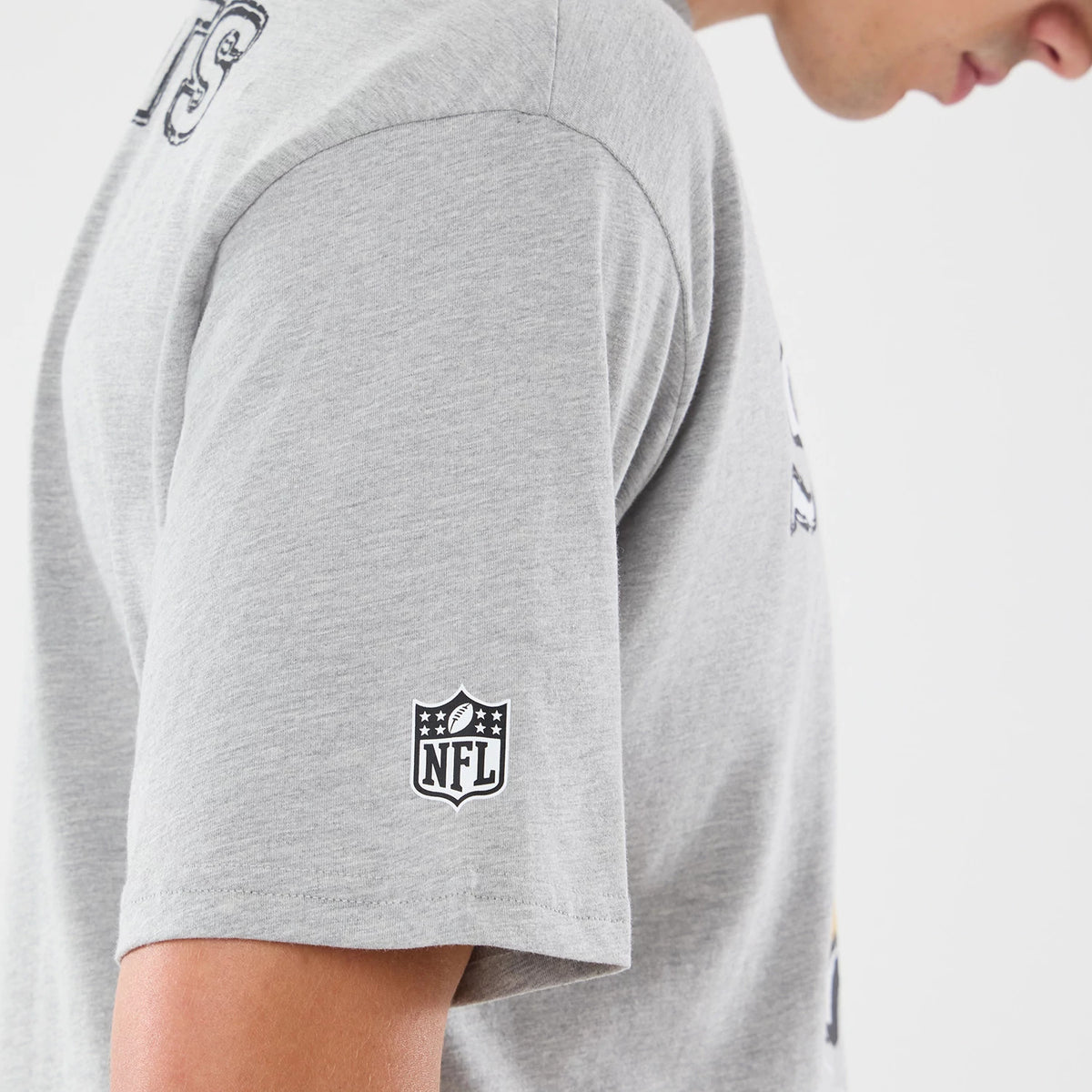 New Era New Orleans Saints NFL Graphic Slogan Grey Oversized T-Shirt, side view on a model showing the grey fabric with a printed NFL logo on the sleeve, view of a graphic slogan on the chest, and relaxed fit sleeve.