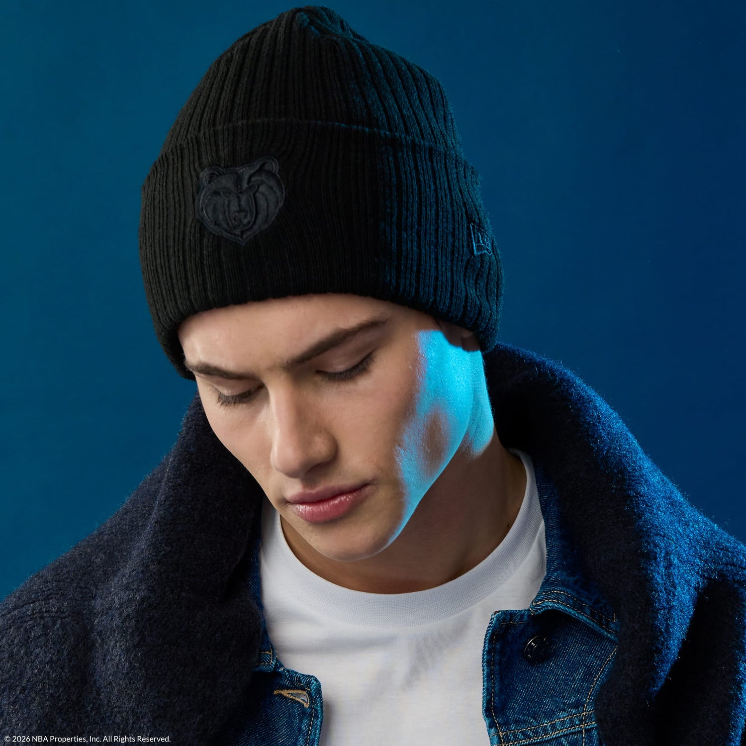 person wearing a black new era NBA beanie hat on a blue background