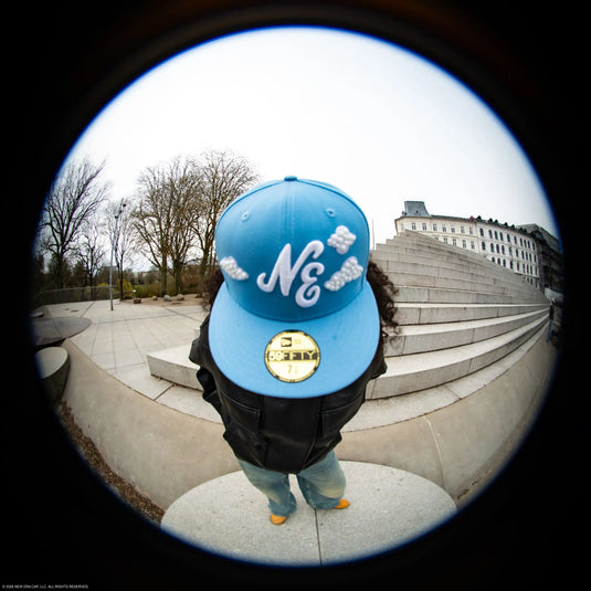 Person wearing a blue new era 59fifty cap with white text standing on steps outdoors.