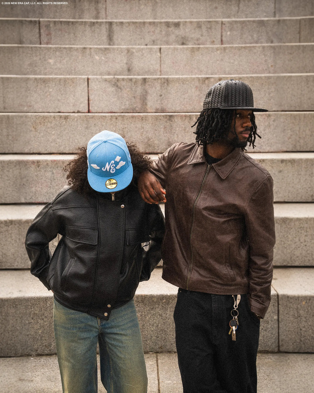 Two people standing on stone steps wearing leather jackets and 59fifty caps.