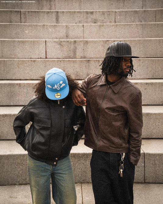 Two people standing on stone steps wearing leather jackets and 59fifty caps.