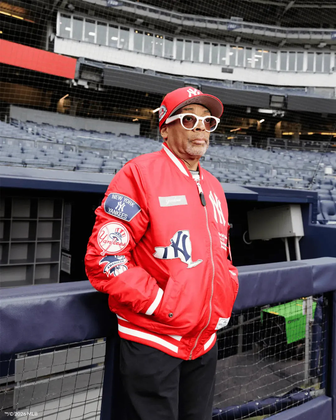 spike lee wearing a red yankees jacket and a red yankees 59fifty cap  standing in a stadium