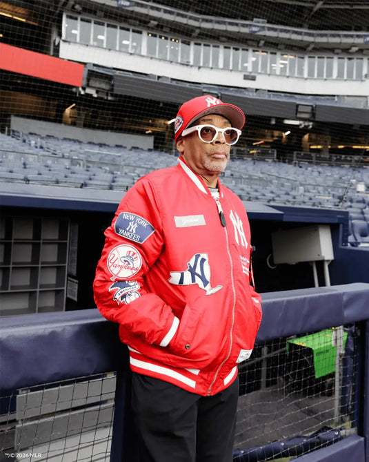 spike lee wearing a red yankees jacket and a red yankees 59fifty cap  standing in a stadium