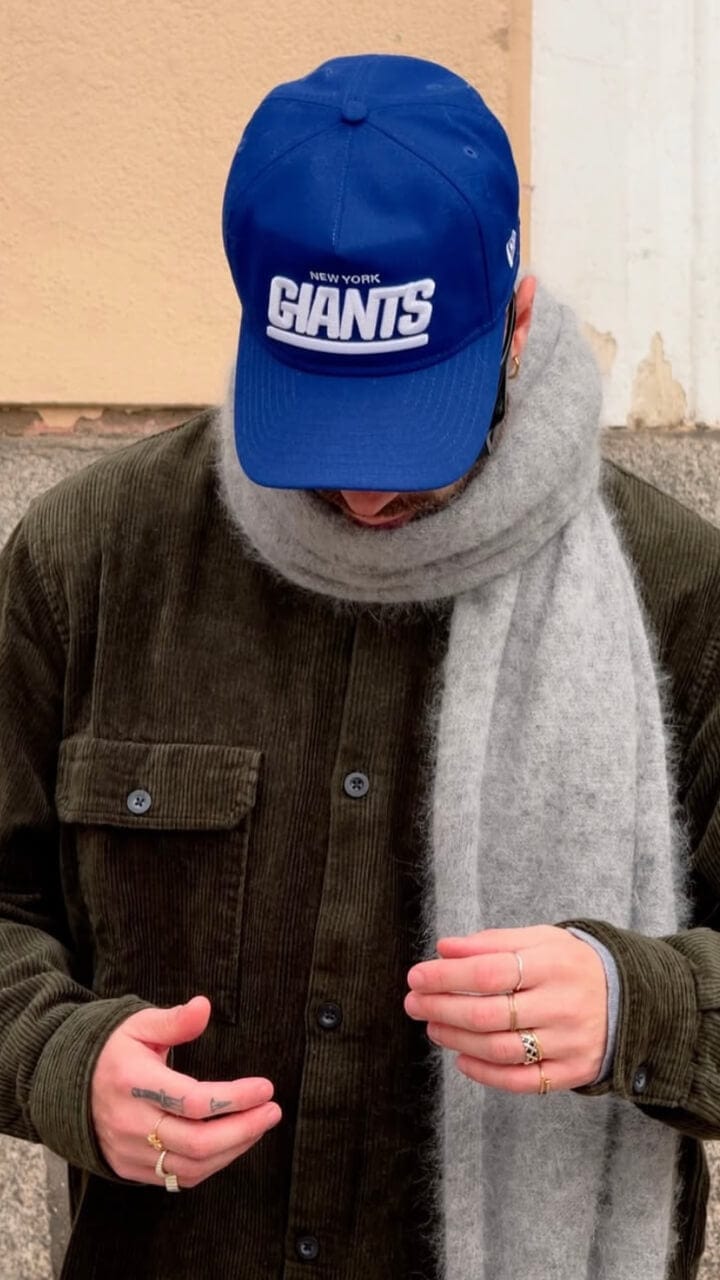 A man wearing a blue New York Giants cap, grey scarf and a green chord jacket.