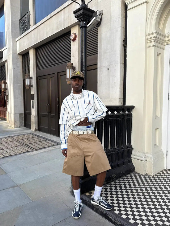 Slide 1:Man standing on a city street wearing a striped shirt, beige shorts, and sneakers.