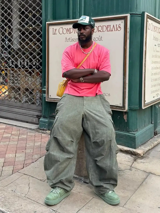 Slide 3:Person wearing a pink shirt and green pants standing in front of a building with signs.