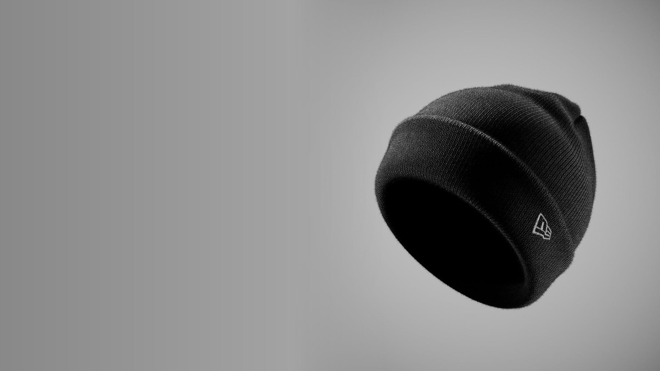 Black new era beanie with a logo on a gray background