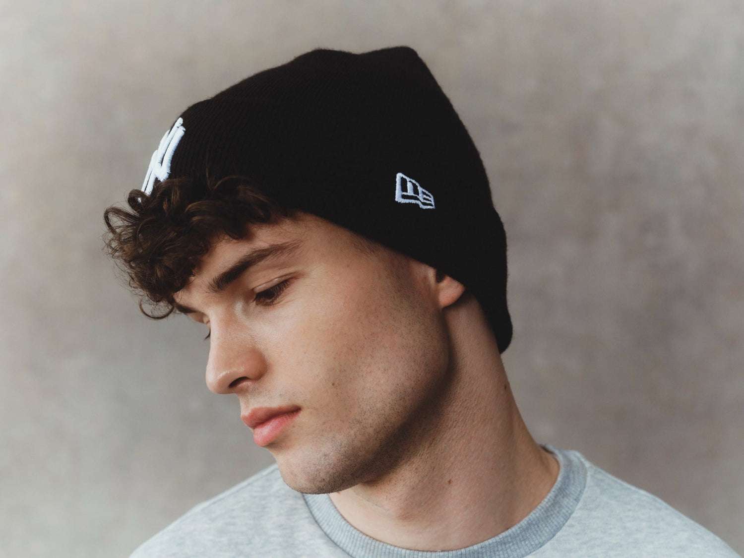 Man wearing a black beanie with New Era logo against a neutral background