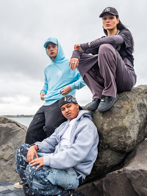 2 men and woman sitting in rocks wearing MLB caps and hoodies