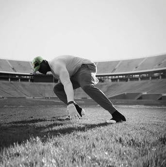 silouhette of a man wearing a green bay packers cap doing shuttle runs on an American football pitch inside a stadium